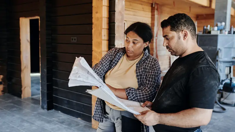 Deux personnes qui consultent ensemble des documents dans une maison en bois en travaux