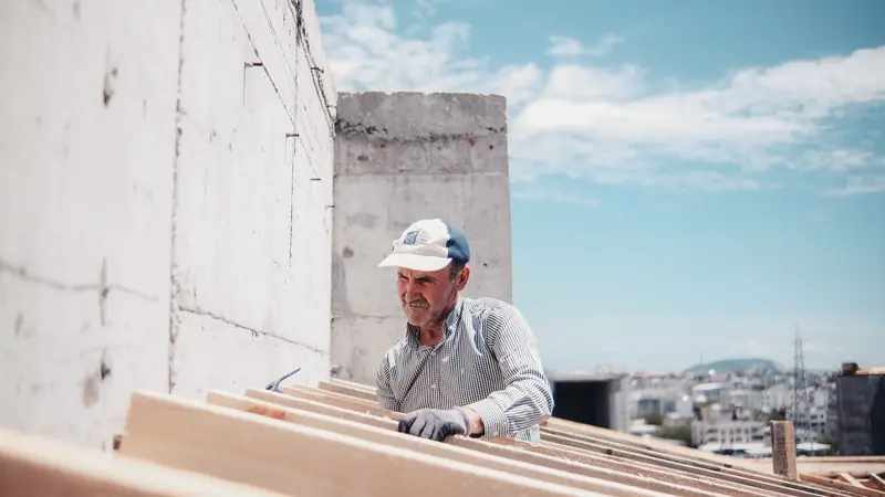 Charpentier en casquette qui pose des chevrons en bois sur un toit en chantier
