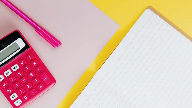Cahier ligné ouvert à côté d'une calculatrice rose et d'un stylo sur fond jaune