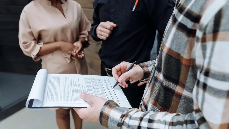 Personne signant un contrat sur un porte-documents devant deux interlocuteurs