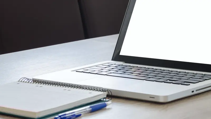 Ordinateur portable ouvert et carnet à spirale posés sur un bureau blanc