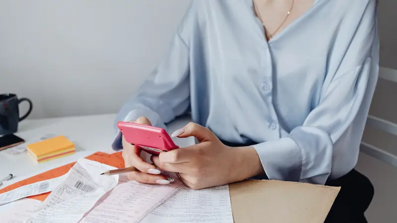 Femme faisant ses comptes avec une calculatrice rose au milieu de factures et de tickets de caisse