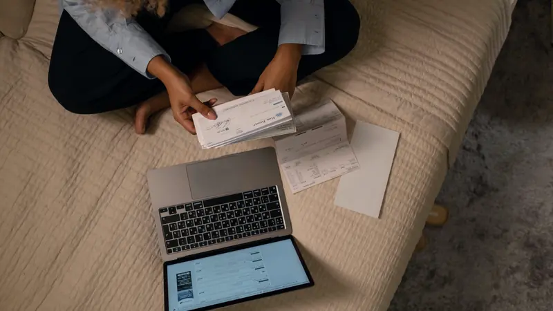 Personne assise sur un lit triant des chèques et des relevés à côté d'un ordinateur portable