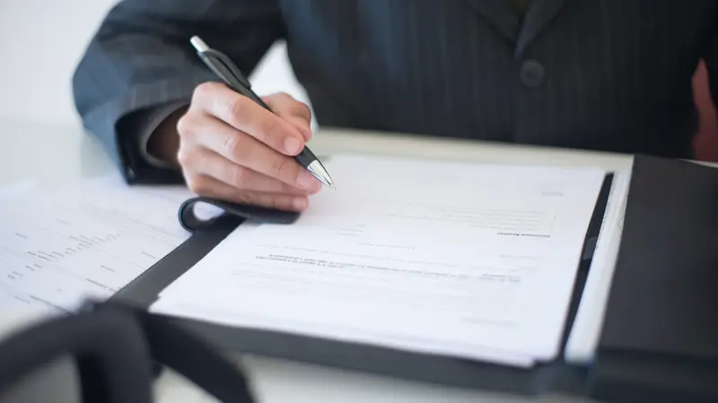 Main remplissant un document posé dans un porte-documents
