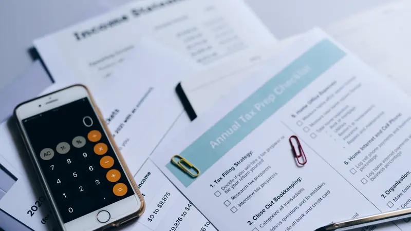 Smartphone affichant une calculatrice posé sur des documents comptables et une liste de contrôle fiscale, avec trombones et stylo