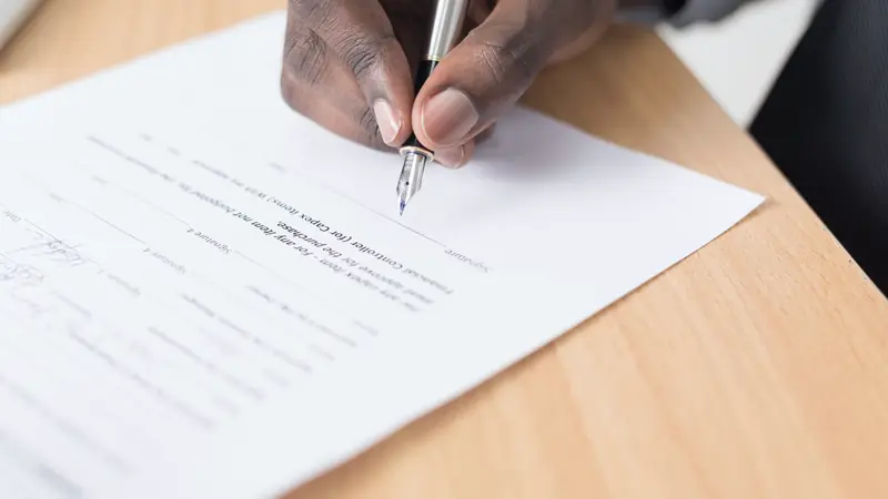 Main signant un document avec un stylo plume sur un bureau en bois