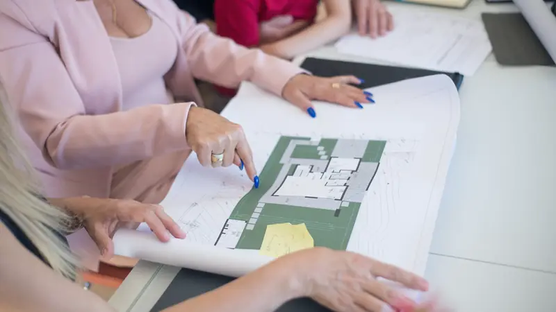 Mains désignant un plan imprimé lors d'une présentation autour d'une table
