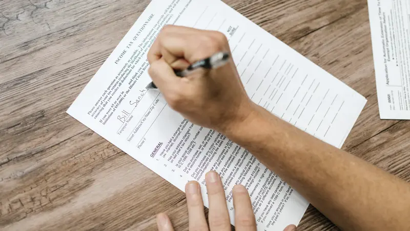 Main remplissant un formulaire administratif sur un bureau en bois