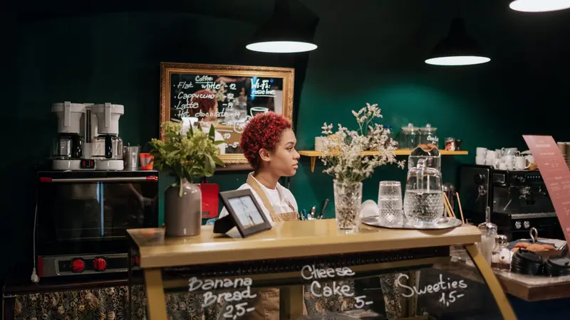 Commerçante derrière le comptoir d'un petit café avec ses tarifs affichés