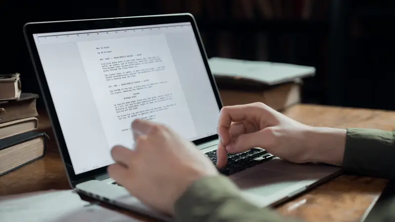 Mains tapant un texte sur un ordinateur portable posé sur un bureau en bois