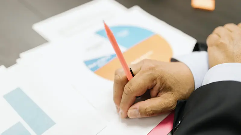 Main tenant un crayon rouge au-dessus de documents financiers imprimés avec des graphiques en secteurs et en barres