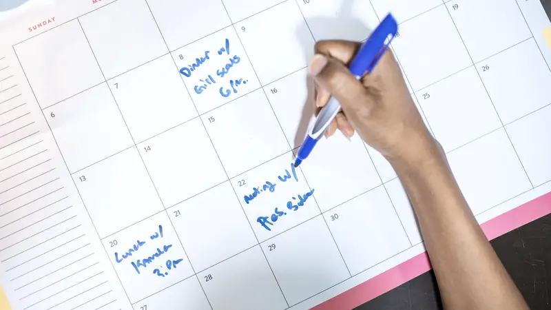Main notant des rendez-vous dans un calendrier mensuel avec un stylo bleu