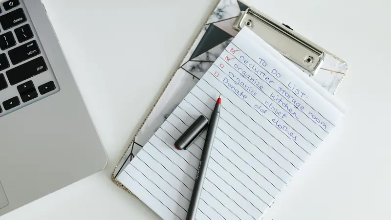 Liste de tâches manuscrite sur un bloc-notes à pince à côté d'un ordinateur portable