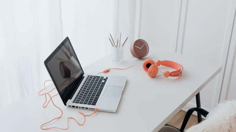 Ordinateur portable, casque orange et petite horloge sur un bureau blanc