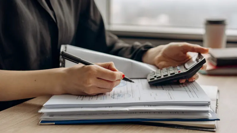 Mains utilisant une calculatrice au-dessus d'une pile de documents comptables