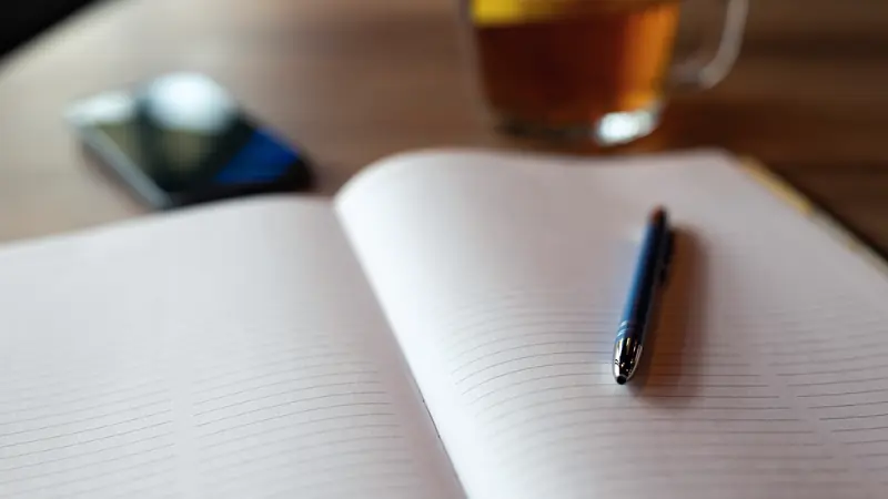 Carnet ouvert, stylo, téléphone et tasse de thé sur un bureau en bois
