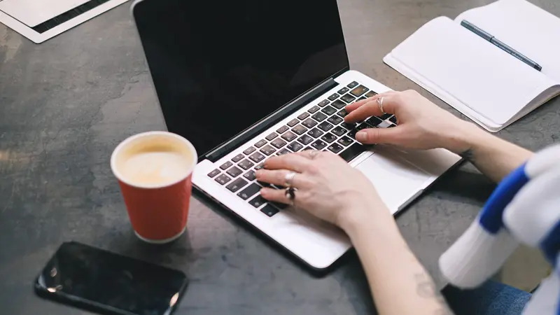 Mains tapant sur un ordinateur portable à une table de café, gobelet à côté