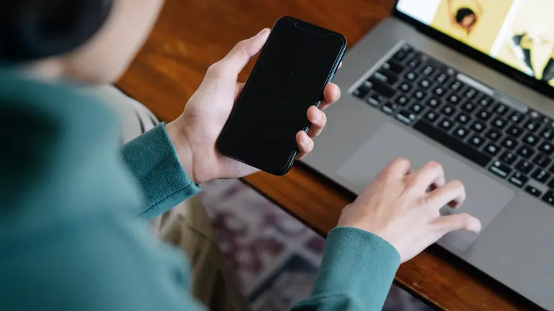 Main tenant un smartphone devant un ordinateur portable ouvert