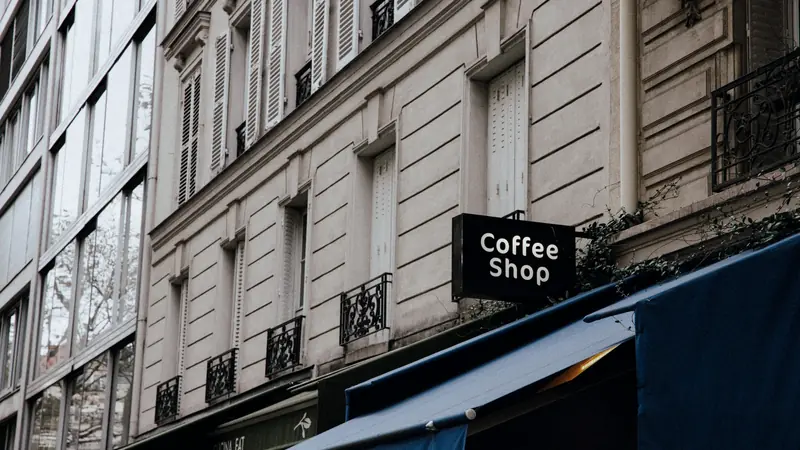 Façade d'immeuble parisien avec une enseigne suspendue Coffee Shop au-dessus d'un store bleu