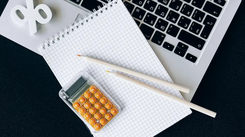 Calculatrice orange posée sur un carnet quadrillé avec deux crayons, devant un clavier d'ordinateur