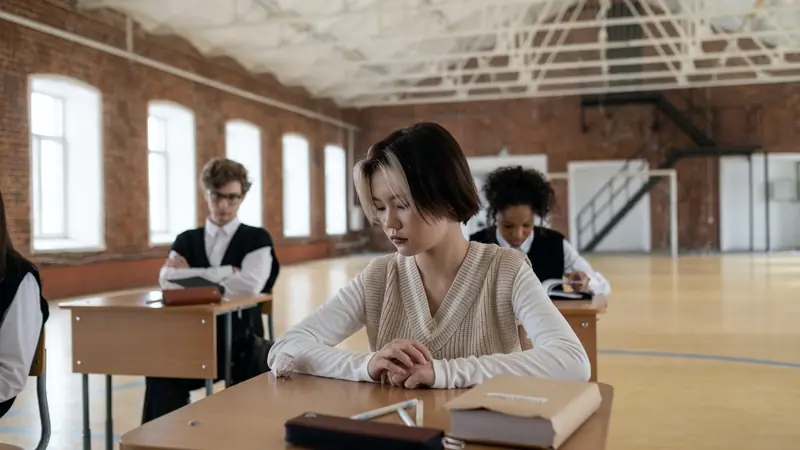 Lycéens assis à des tables individuelles espacées dans une grande salle aux murs de briques, comme lors d'une épreuve écrite