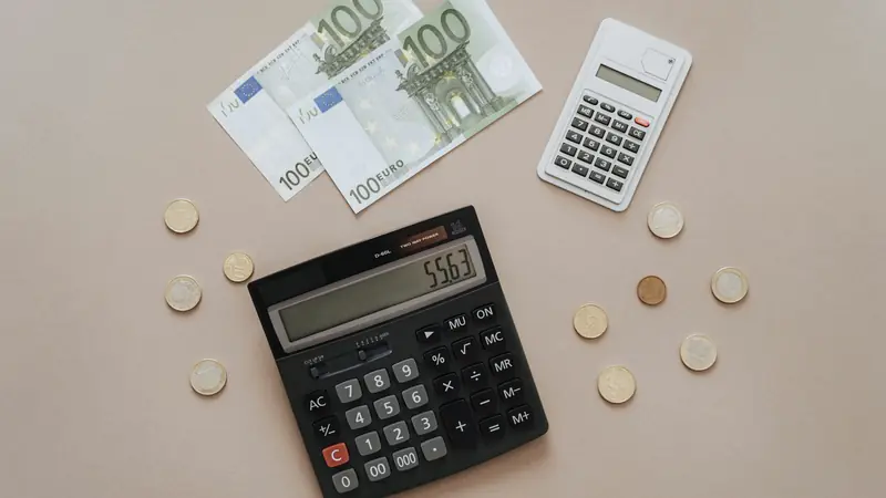 Billets en euros, pièces et calculatrices sur une table beige