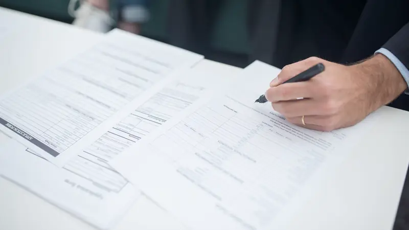 Main signant un contrat parmi plusieurs documents posés sur un bureau