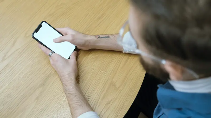 Mains tenant un smartphone au-dessus d'une table en bois