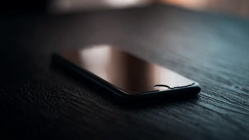 Smartphone noir posé à plat sur une table sombre, écran éteint, dans une lumière tamisée