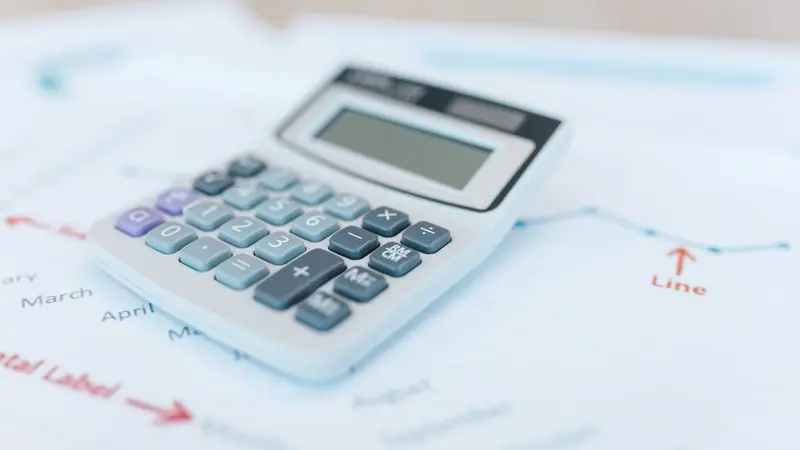 Calculatrice de bureau grise posée sur des feuilles imprimées de graphiques financiers
