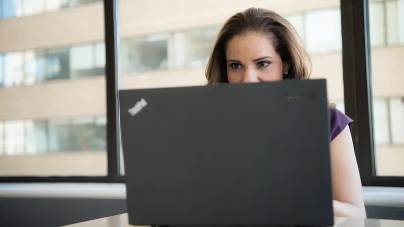 Femme travaillant sur un ordinateur portable noir devant une baie vitrée de bureau