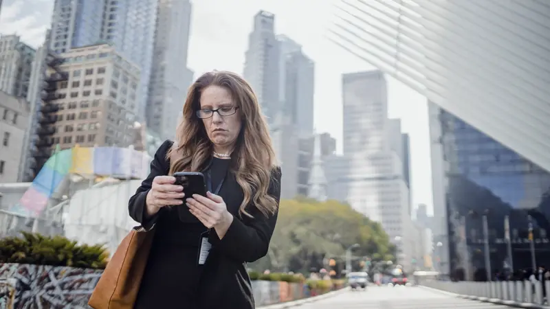 Femme en tenue sombre consultant son smartphone dans une rue bordée d'immeubles